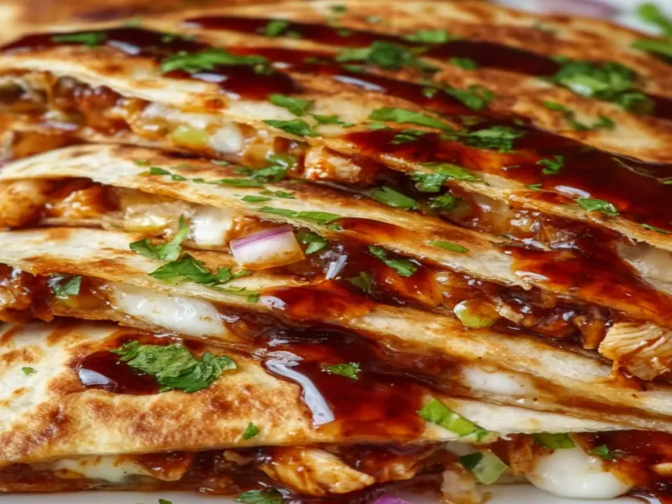 Stacked wedges of griddled flour tortilla quesadilla browned in blistered patches with shredded chicken and melted cheese, drizzled with dark glossy sauce and scattered with red onion and herbs