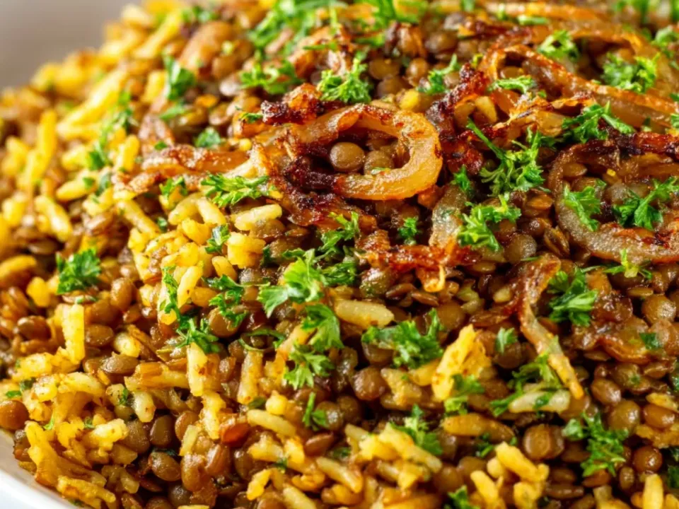A platter of brown-green lentils mixed with golden yellow long-grain rice, topped with dark caramelized onion rings and chopped parsley