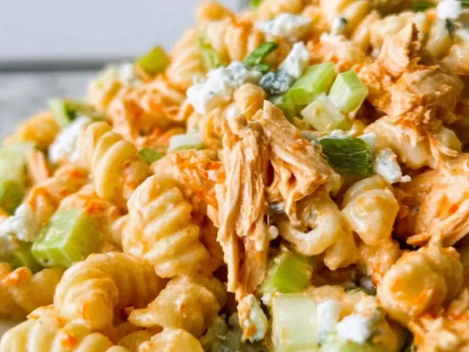 Cavatappi in a creamy orange dressing piled on a white plate with shredded buffalo chicken, crumbled blue cheese, diced celery, scallion and torn lettuce, served cold