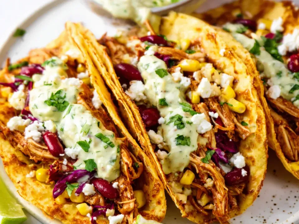Lightly griddled corn tortillas filled with shredded spiced chicken, sweet corn, red kidney beans and purple cabbage, topped with crumbled white cheese, coriander and a pale green crema