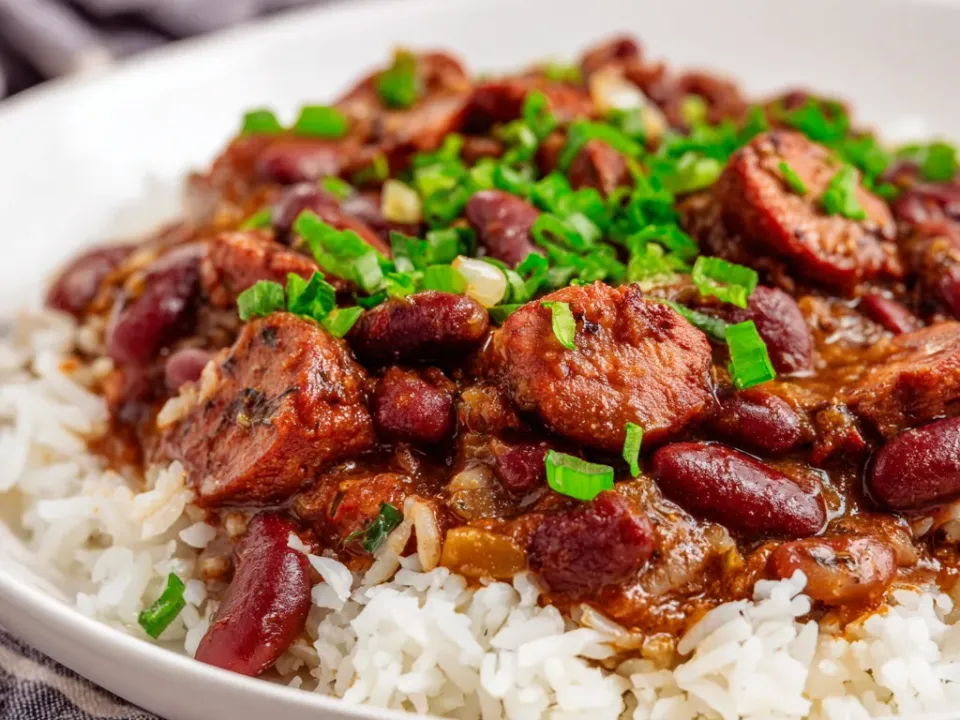 Whole red kidney beans and browned sausage slices in a thick gravy spooned over white rice, scattered with sliced green onions