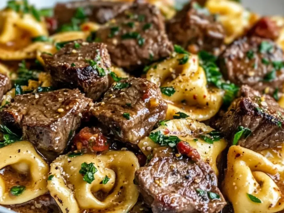 Cheese tortellini with browned steak cubes in a glossy buttery herb sauce with parsley and red chilli flecks on a white plate