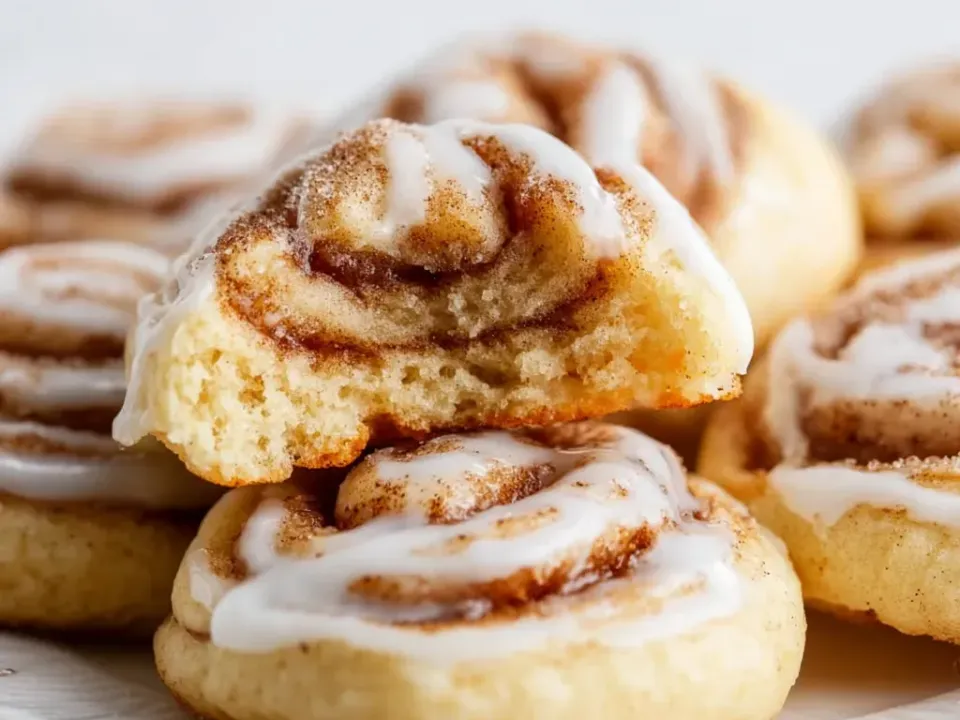 Thick soft cookies with a cinnamon-sugar swirl on top under a white glaze spiral, one bitten to show a soft crumb