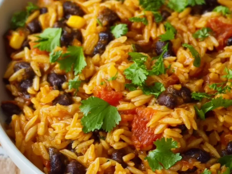 A white bowl of orzo in a red-orange taco-seasoned sauce with black beans, diced tomato, corn kernels and fresh cilantro leaves