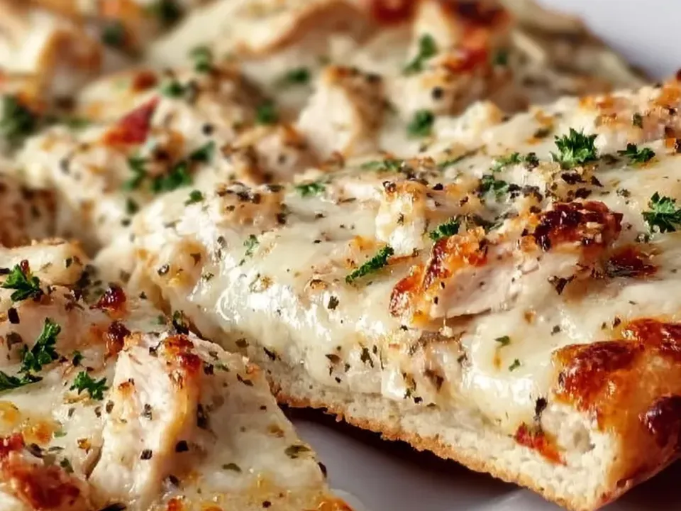 Slices of pizza on a white plate with a white garlic-ranch base, chicken pieces, melted mozzarella and heavy dried herbs, with no red sauce